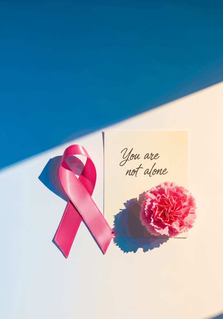 A pink ribbon, a carnation, and a card with 'You are not alone' text on a gradient blue and white background, symbolizing support