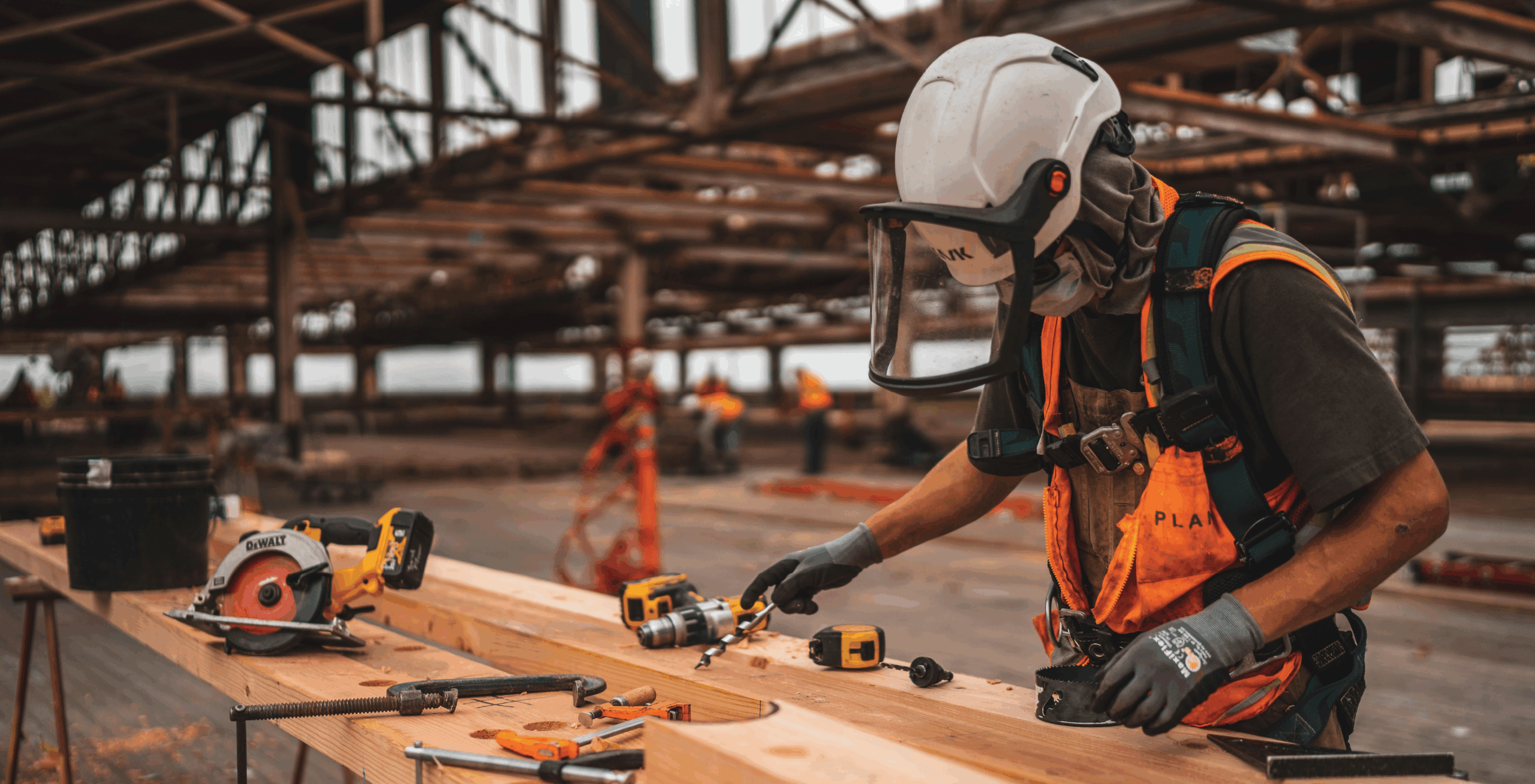 Construction worker in safety gear measuring or prepping a wooden beam with power tools on a construction site