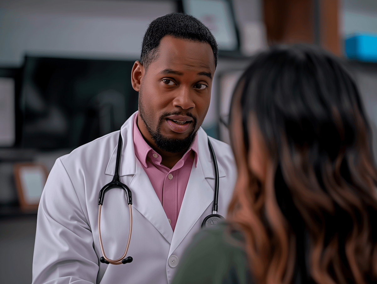 A doctor attentively listens to a patient in a medical office, wearing a white coat and stethoscope.