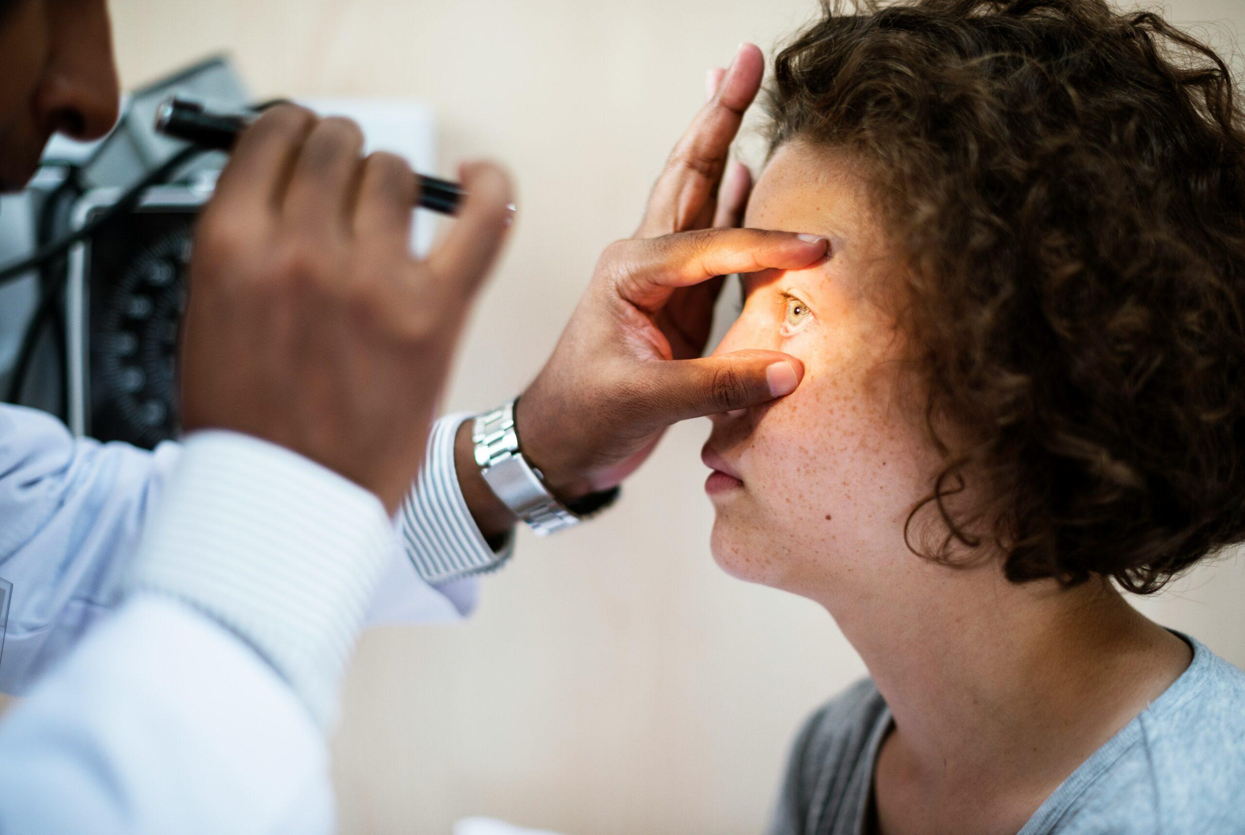 A healthcare professional examining a patient’s eye up close, gently holding the eyelid open while shining a bright light to check the eye’s response and condition.