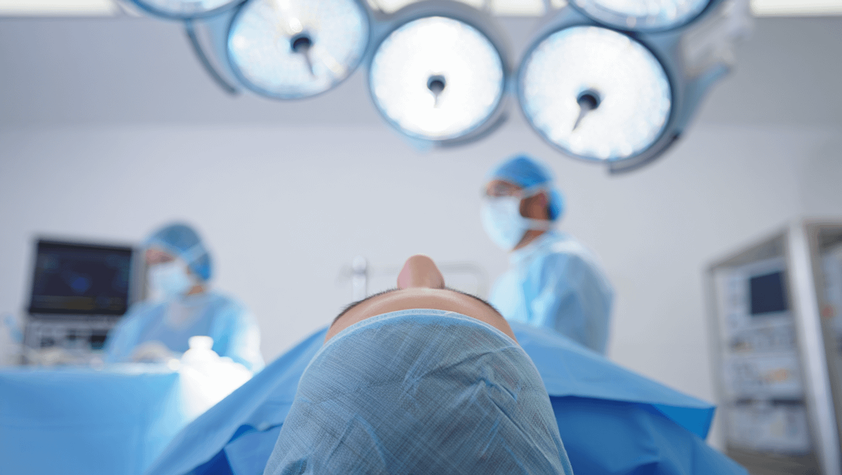 Patient's view in an operating room with surgeons in blue scrubs, bright surgical lights, and medical equipment in a sterile setting