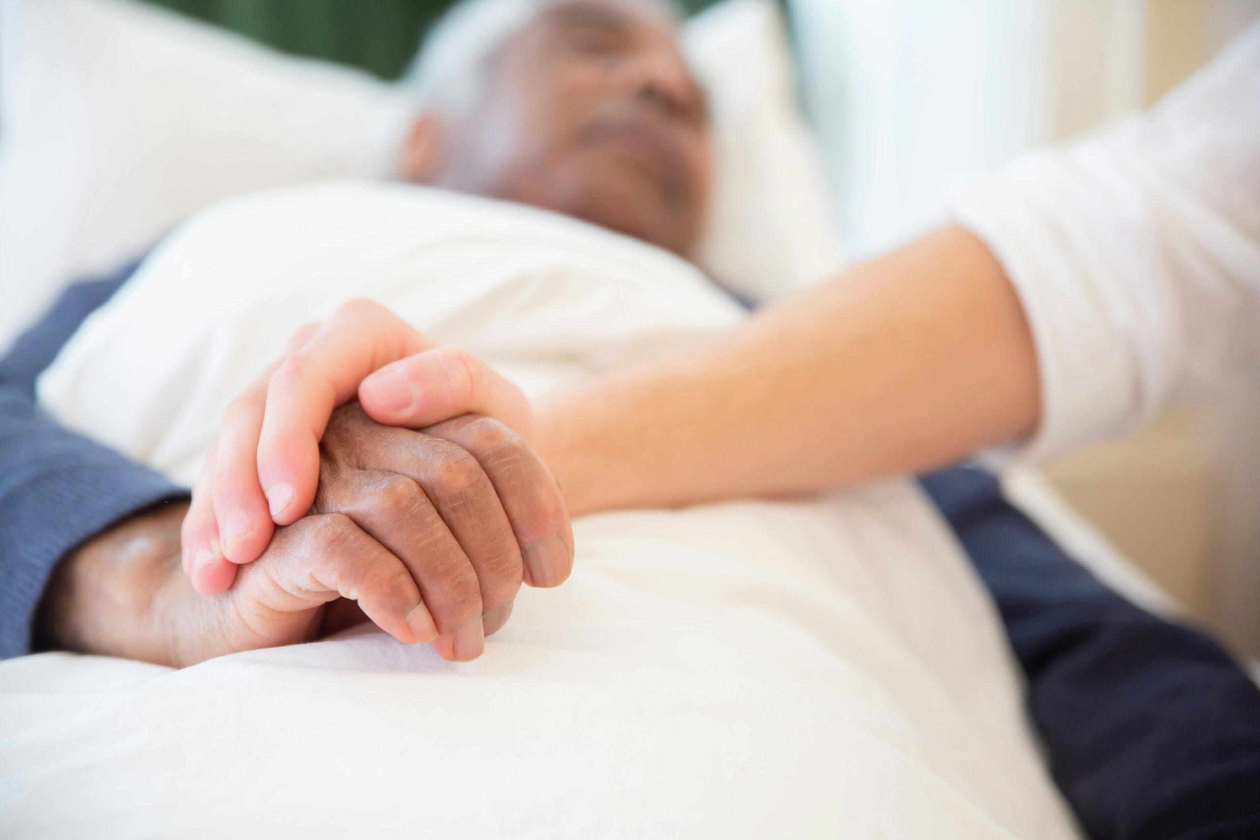 older man holding woman's hand in hospital bed